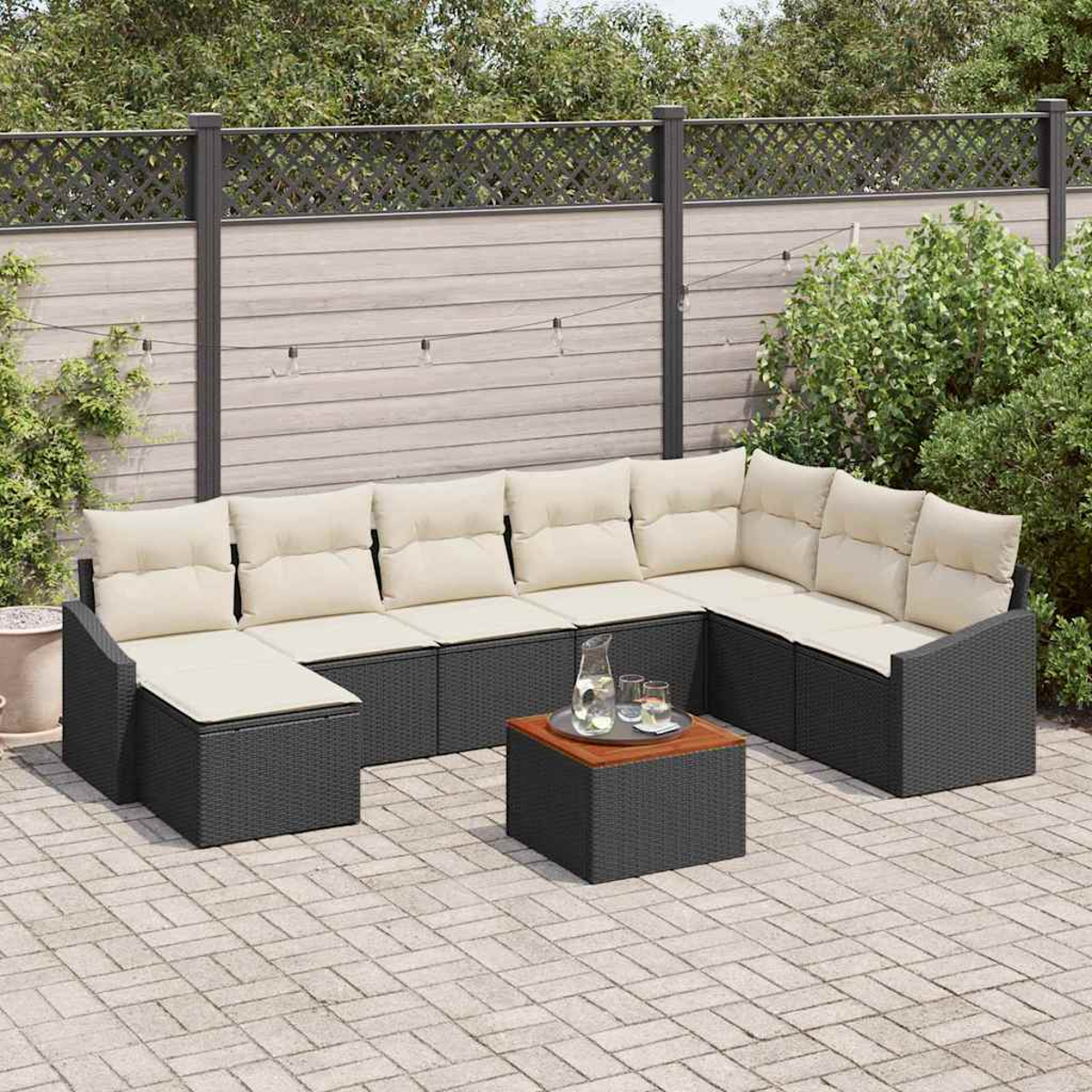 Garten-Sofa-Set: dunkelgraues Korbmöbel mit cremefarbenen Kissen, kleiner Tisch und Ziegel-Terrasse. Holzzaun und Grün im Hintergrund.