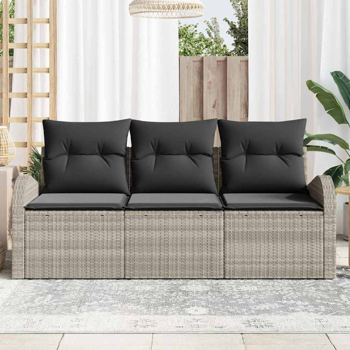 Ein graues Rattan-Sofa mit drei Kissen und Kissen. Dahinter sind weiße Vorhänge und ein Fenster zu sehen.