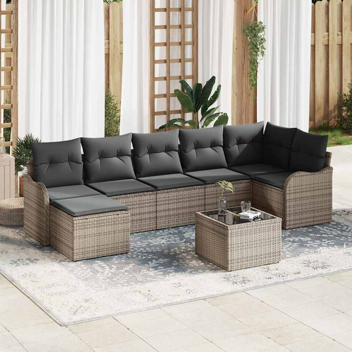 Ein Ecksofa aus Korbgeflecht mit grauen Kissen und einem Couchtisch mit Glasplatte steht auf einem gemusterten Teppich.