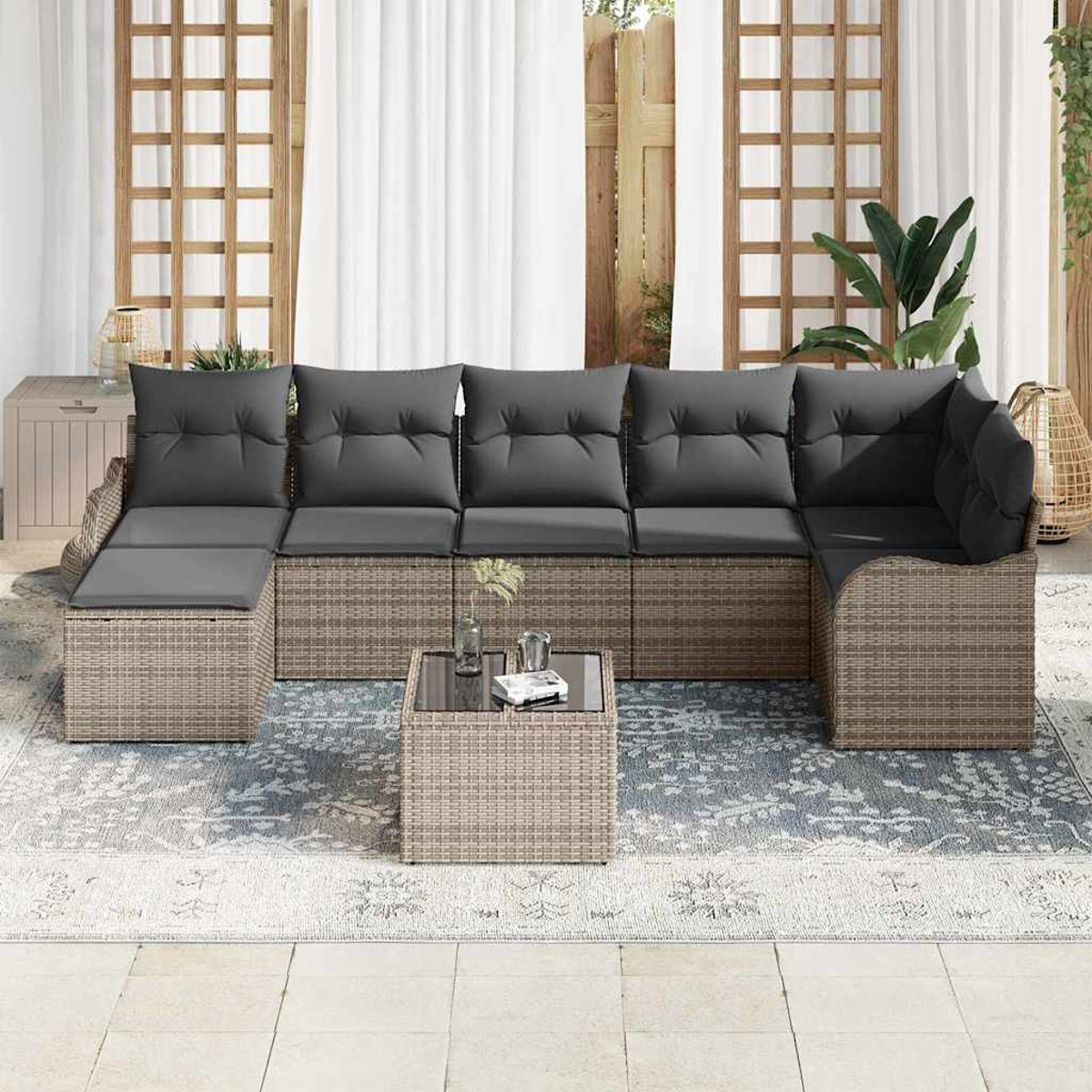 Outdoor-Ecksofa mit grauen Kissen und einem Couchtisch mit Glasplatte auf einem gemusterten Teppich, in der Nähe eines Fensters.
