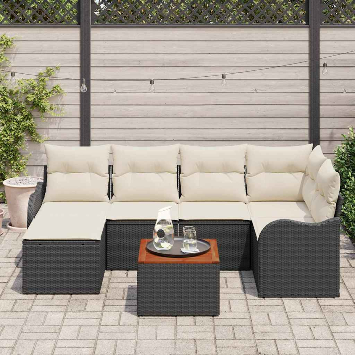 Sofá seccional exterior con cojines crema, marco de mimbre negro y mesita, contra una valla de madera.