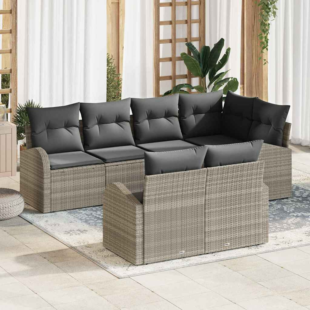 Outdoor-Sofa aus Korbgeflecht mit grauen Kissen. Weiße Vorhänge und Holzgitter im Hintergrund. Pflanzen sind sichtbar.