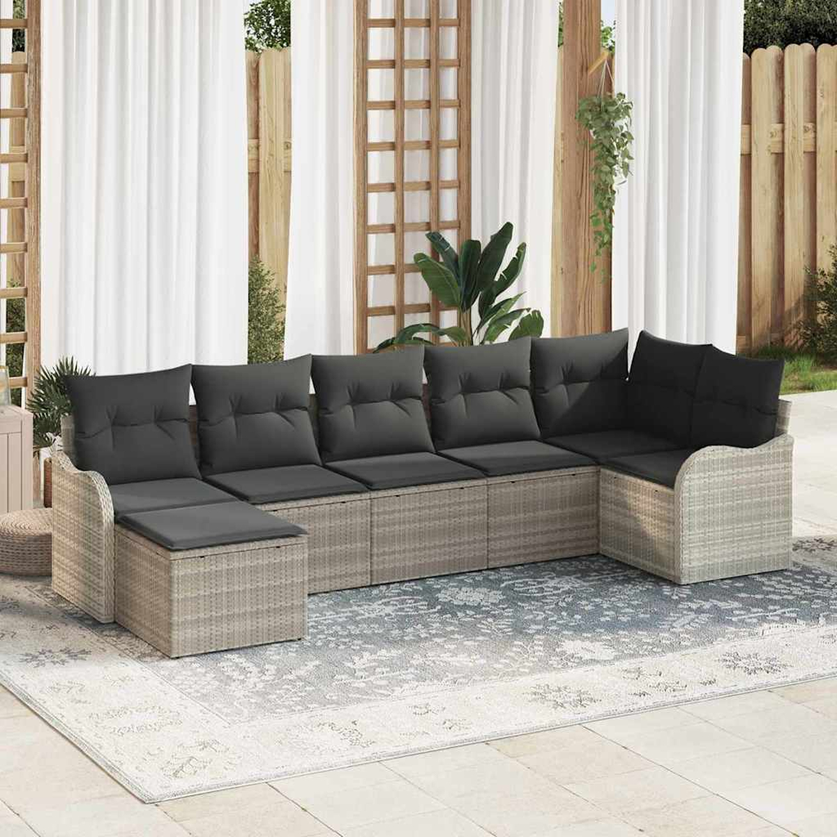 Outdoor-Ecksofa mit grauen Kissen auf einem gemusterten Teppich, weißen Vorhängen und einem Holzzaun im Hintergrund.