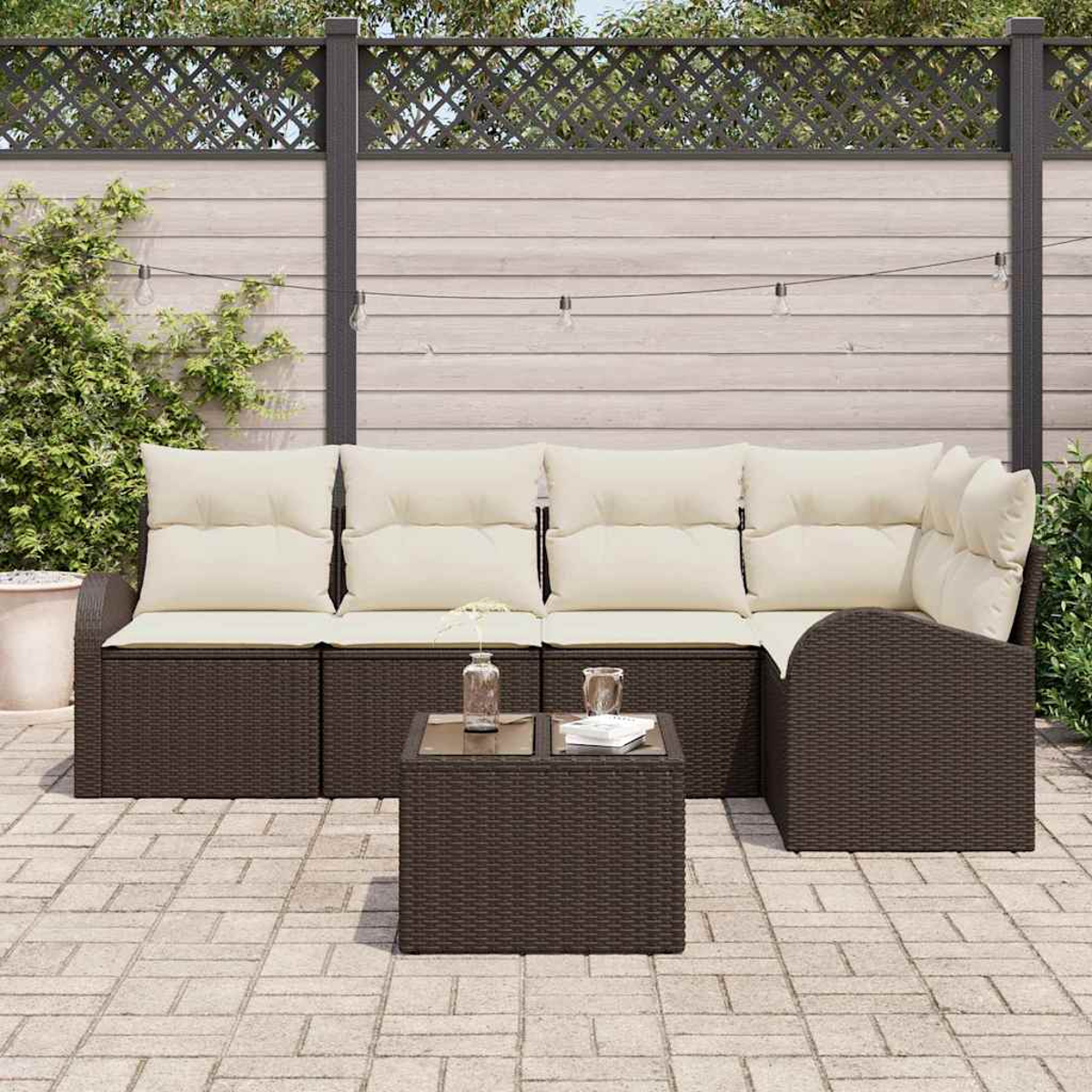 Gartenmöbel: braunes Korbmöbel mit cremefarbenen Kissen, kleiner Tisch, auf Steinboden, mit Zaun.