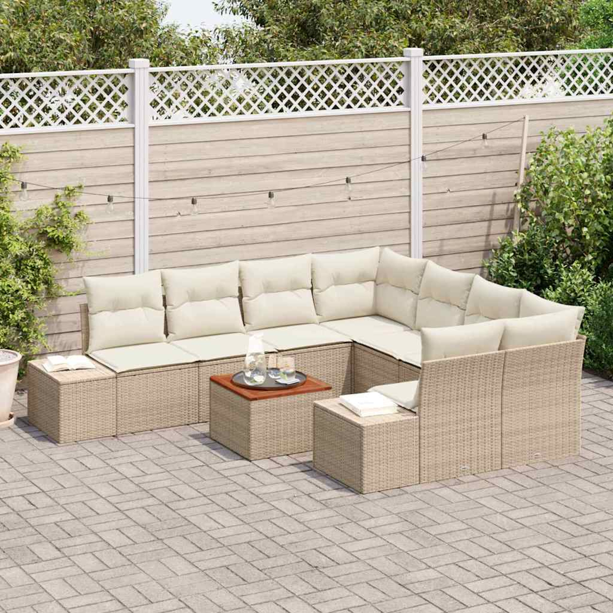 Beiges Outdoor-Rattan-Sofa-Set mit cremefarbenen Kissen, zwei kleinen Tischen, Getränken und einem weißen Gitterzaun im Hintergrund.