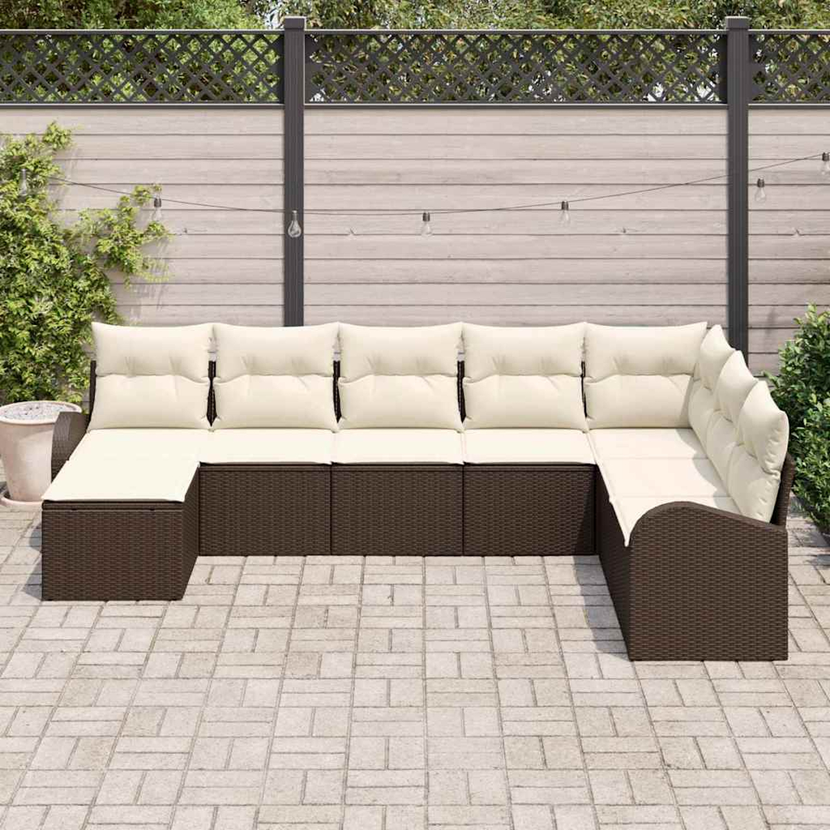 Ein Ecksofa im Freien mit beigefarbenen Kissen und braunem Korbbasiss steht auf einer Steinveranda. Ein Zaun und Grünzeug sind im Hintergrund.