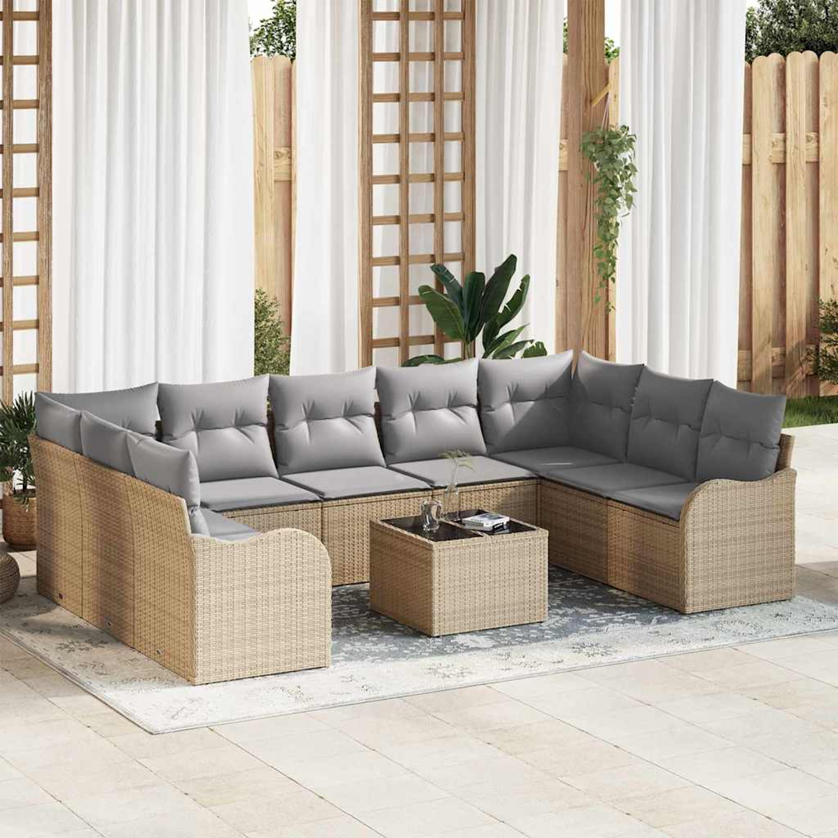 Ein Outdoor-Wicker-Sofa mit grauen Kissen und einem passenden Couchtisch auf einem Teppich. Hintergrund: Vorhänge, Holzzaun und Pflanzen.