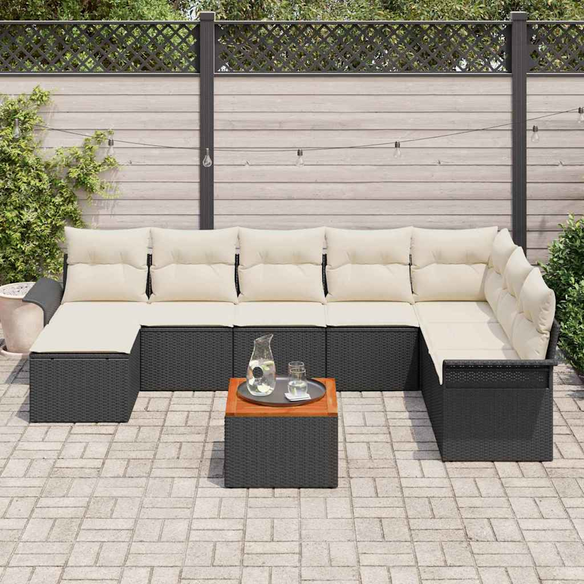 Outdoor-Ecksofa mit cremefarbenen Kissen und einem kleinen Tisch. Auf dem Tisch stehen ein Krug und ein Glas auf einem Tablett. Holzzaun im Hintergrund.