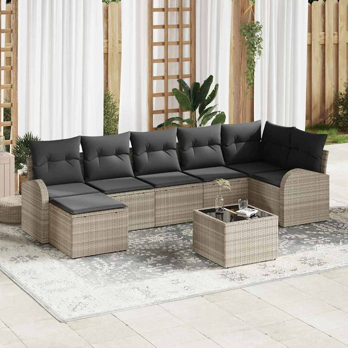 Gartensofa mit grauen Kissen und Glastisch. Auf einem Teppich vor Vorhängen und Holzzaun.