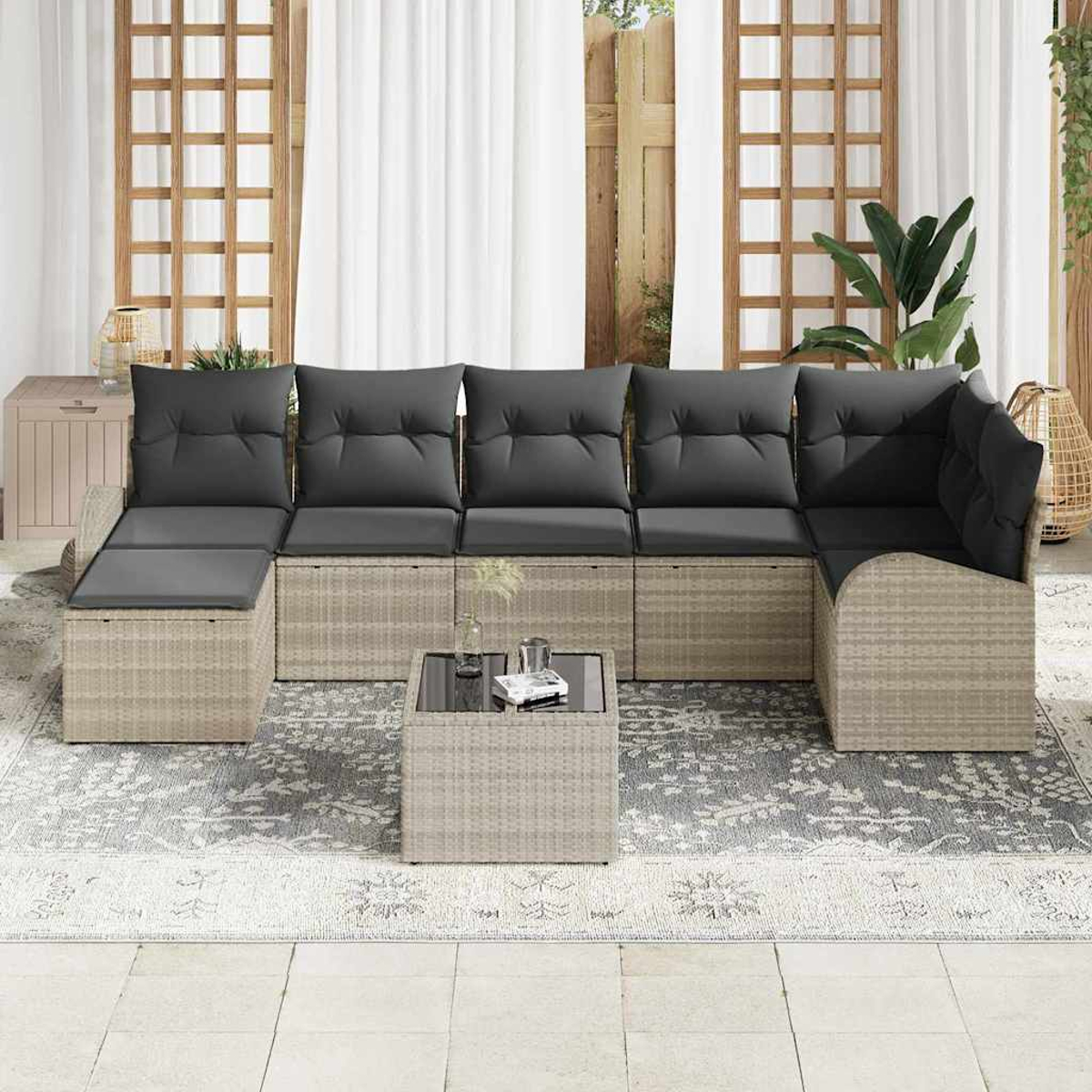 Outdoor-Ecksofa mit grauen Kissen auf gemustertem Teppich. Kleiner Glastisch davor. Holzgitter und weiße Vorhänge im Hintergrund.
