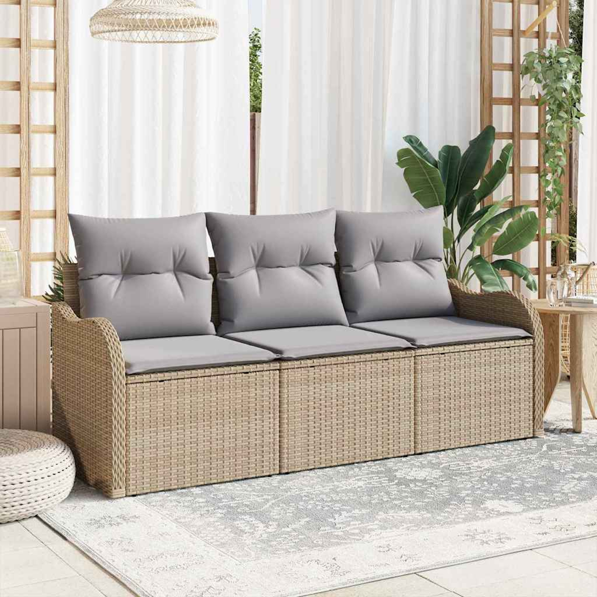 Ein Korbmöbelsofa mit drei grauen Kissen steht auf einem gemusterten Teppich. Rechts befinden sich eine Pflanze und ein Spalier; weiße Vorhänge im Hintergrund.