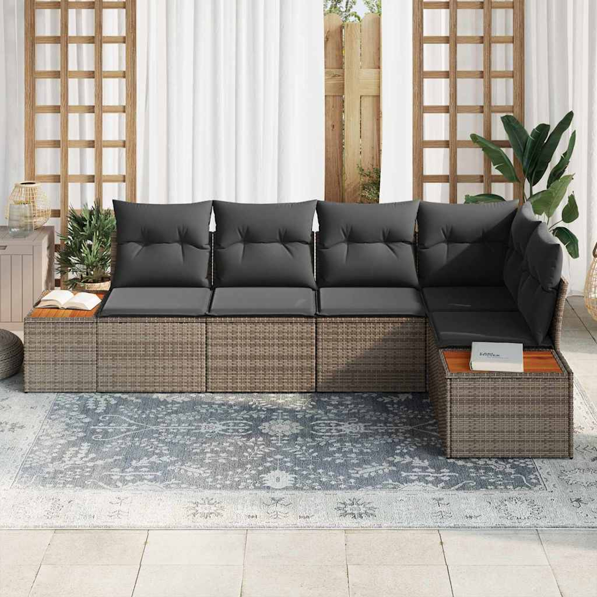 Ein Ecksofa aus Rattan mit grauen Kissen steht auf einem Teppich. Vorhänge und Holzgitter im Hintergrund.