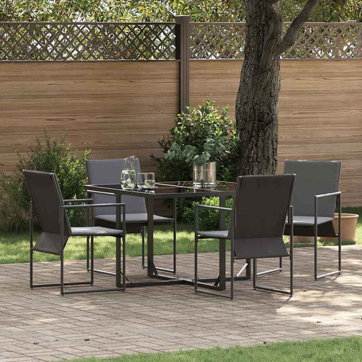Essgarnitur im Freien mit Glastisch, vier Stühlen und Getränken. Auf einer Terrasse mit Holzzaun und Grün.