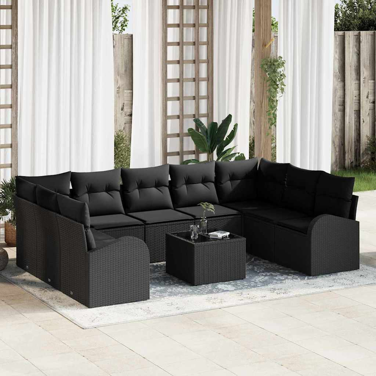 Sofá seccional de mimbre negro para exteriores con cojines y una mesa de centro cuadrada a juego en un patio con cortinas blancas.