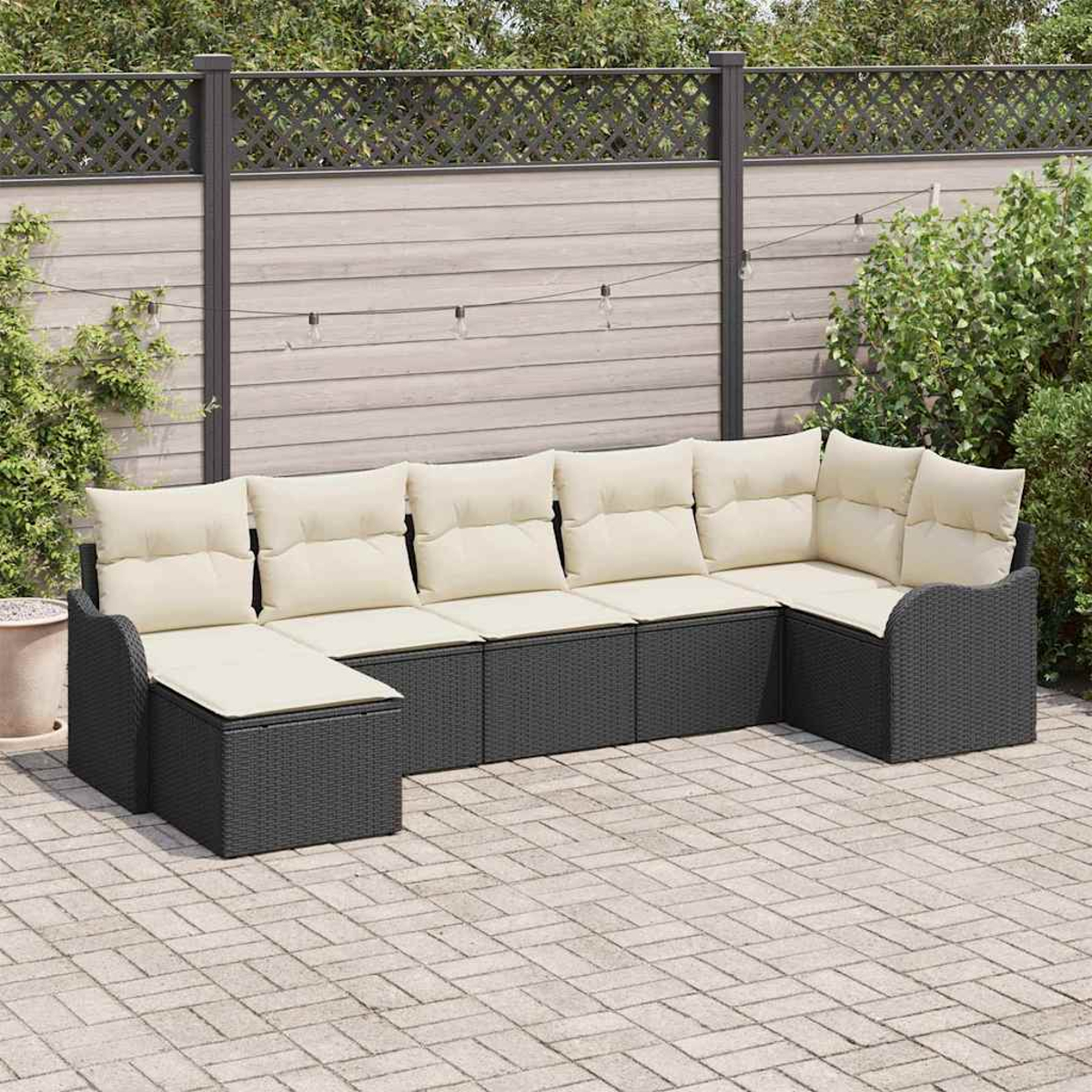 Ein U-förmiges Outdoor-Sofa mit cremefarbenen Kissen steht auf einer Ziegelterrasse. Ein Zaun und Grün bilden den Hintergrund.