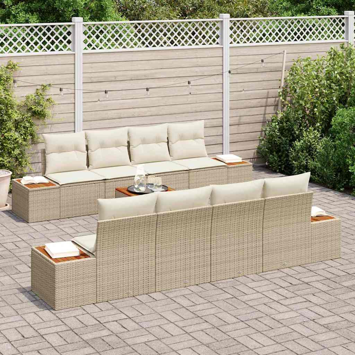 Outdoor-Sitzgruppe mit beigen Kissen, einem Holztisch und einem weißen Zaun im Hintergrund auf einer gepflasterten Terrasse.