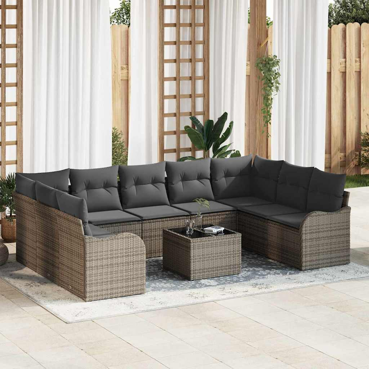 Outdoor-Sitzgruppe mit grauen Kissen auf einer Terrasse. Enthält einen Couchtisch. Hintergrund: weiße Vorhänge und Holzzaun.