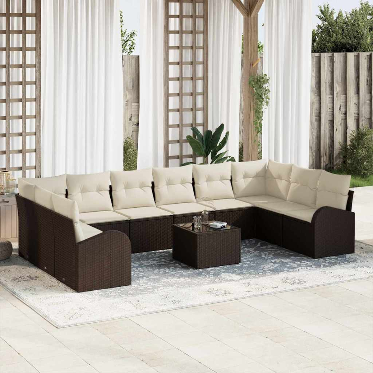 Ein Ecksofa mit cremefarbenen Kissen und braunem Korbgewebe. Davor steht ein kleiner quadratischer Tisch. Weiße Vorhänge und ein Holzgitter.
