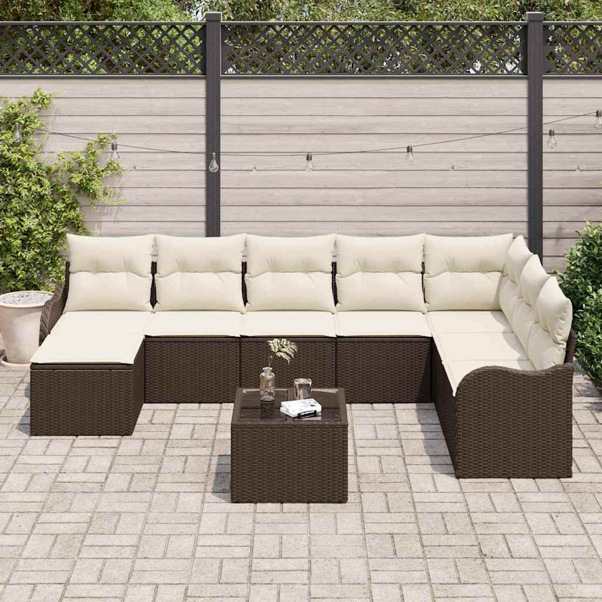 Outdoor-Ecksofa mit cremefarbenen Kissen und einem braunen Korbgeweberahmen, kleiner quadratischer Couchtisch und Gartenzaun im Hintergrund.