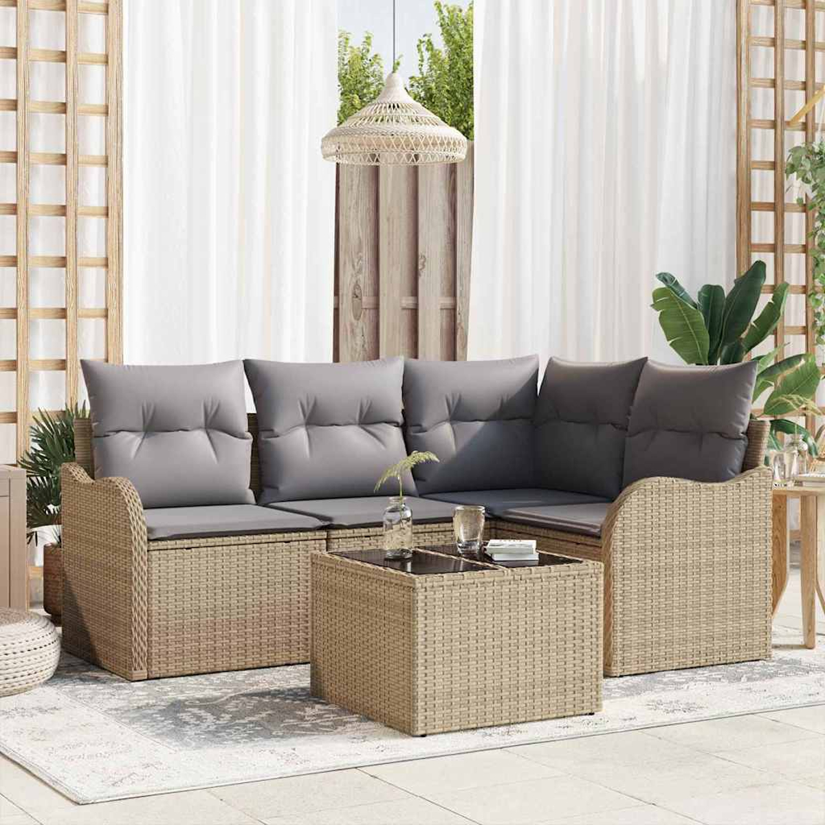 Outdoor-Korbmöbelset mit grauen Kissen und einem Couchtisch mit Glasplatte. Weiße Vorhänge und Grünzeug sind im Hintergrund.