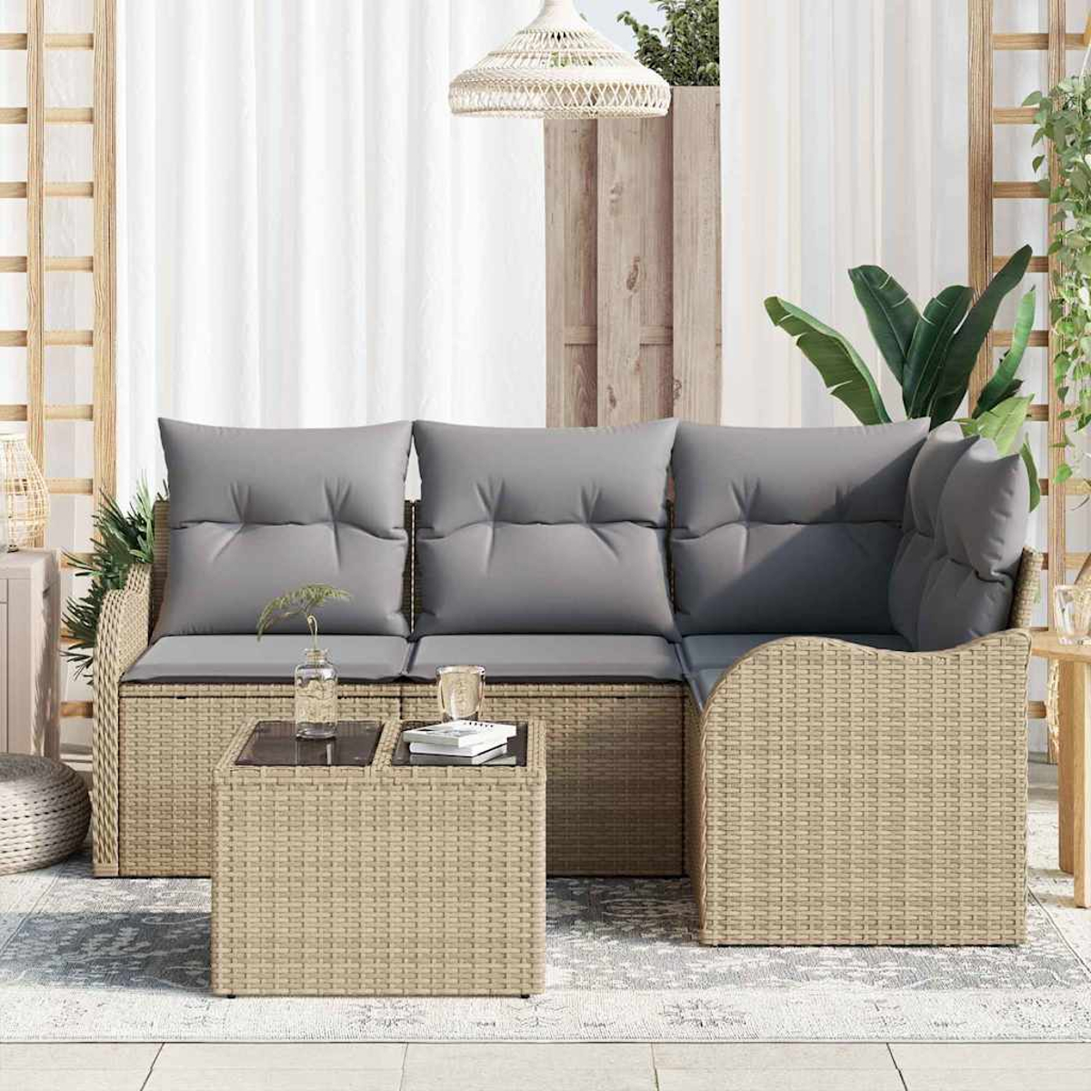 Geflochtene Outdoor-Couch mit grauen Kissen. Vorne steht ein kleiner Tisch mit Glasplatte und Büchern. Weiße Vorhänge und Pflanzen im Hintergrund.