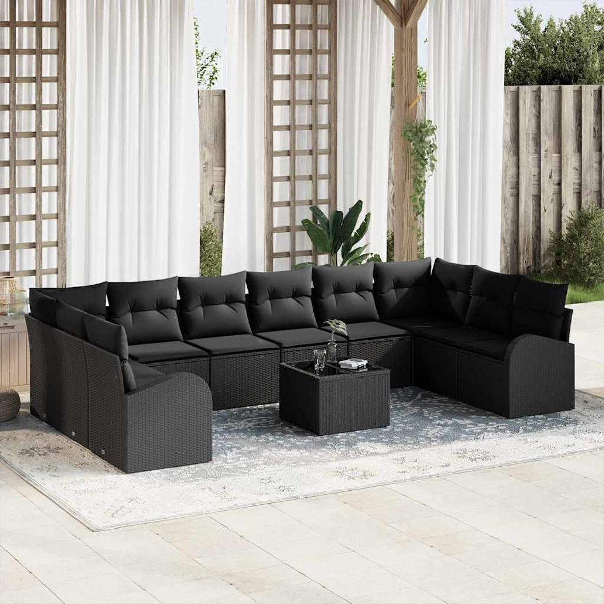 Schwarzes Korbsessel-Sofa mit Kissen und einem kleinen Tisch. Weiße Vorhänge und eine Holzkonstruktion im Hintergrund.