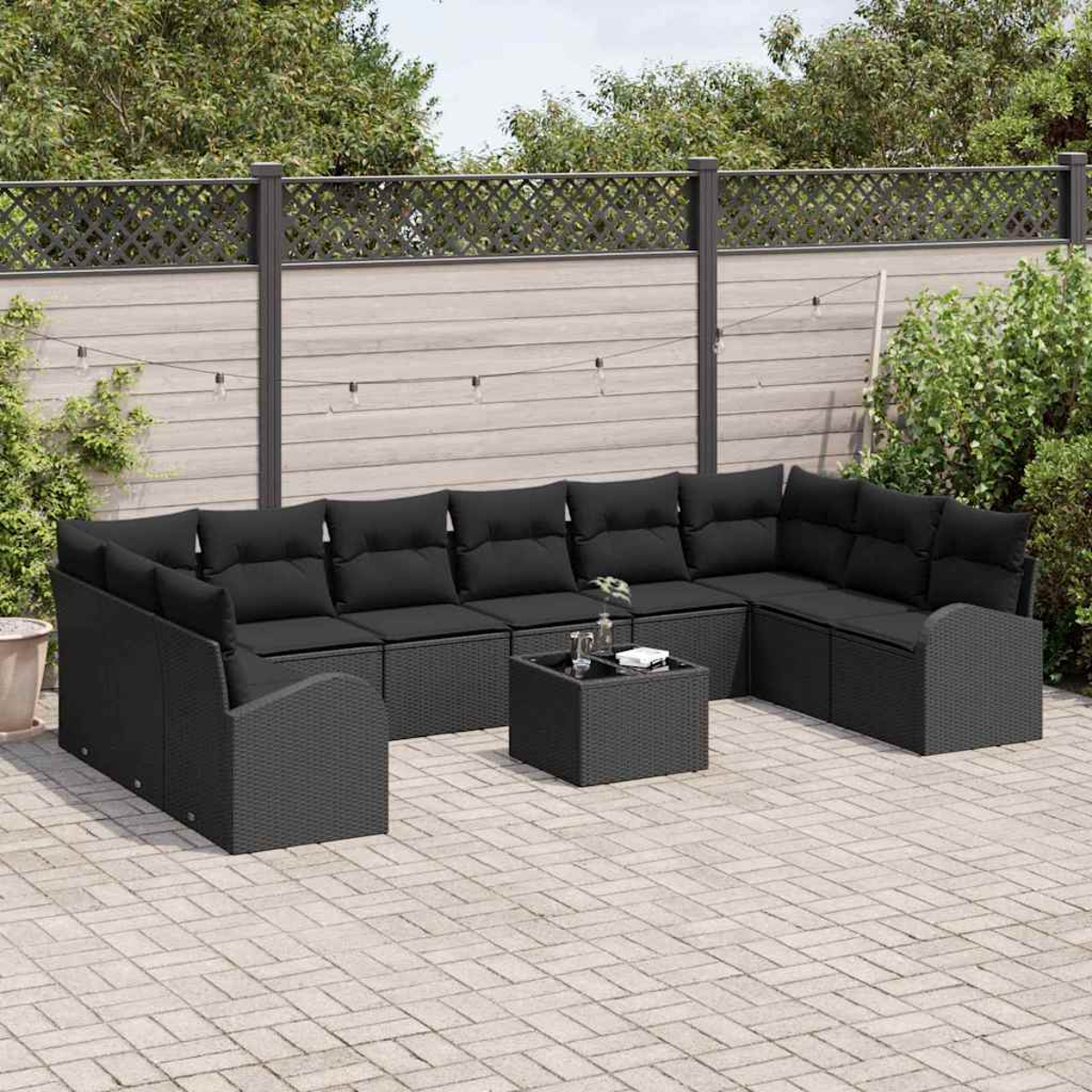 Schwarzes Outdoor-Rattan-Sofagarnitur mit schwarzen Kissen und einem quadratischen Tisch auf einer gepflasterten Terrasse.
