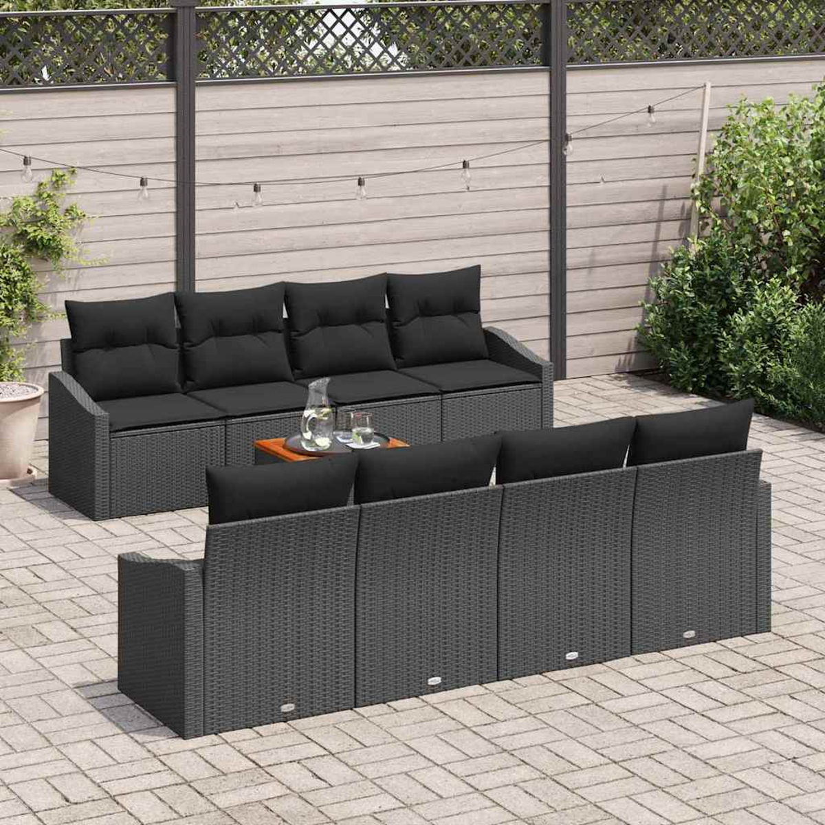 Garten-Set mit grauem Korbsessel, schwarzen Kissen und Holztisch. Die Szene hat einen Holzzaun, Lichter und Grün.