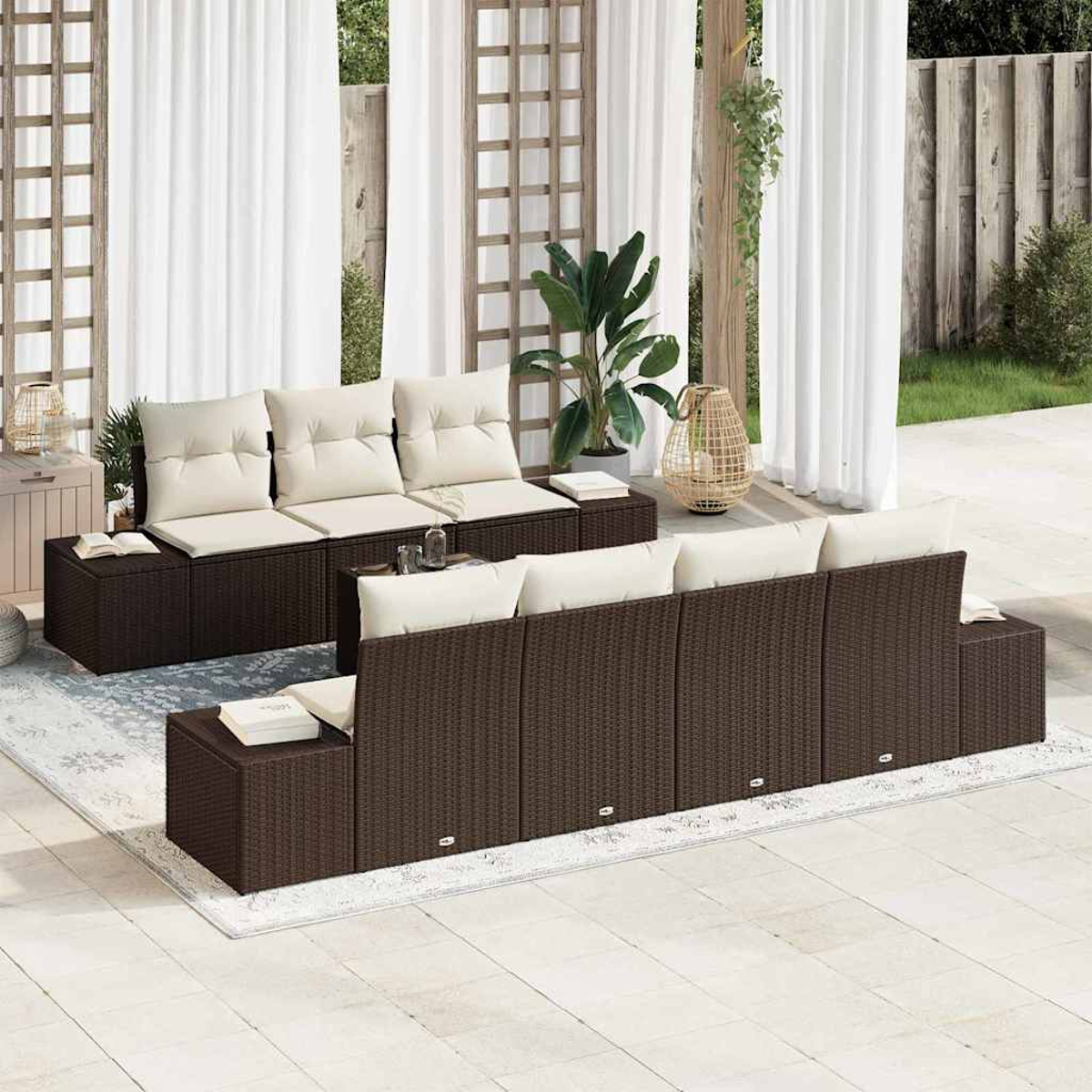 Garten-Terrassen-Set mit braunen Korbmöbeln, weißen Kissen und einem Teppich. Im Hintergrund Vorhänge, Pflanzen und ein Holzgitter.