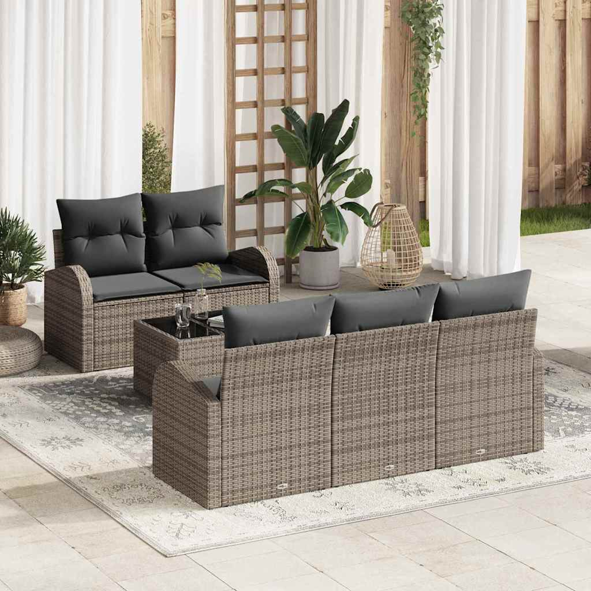 Terrasse mit Rattansitzmöbeln, grauen Kissen und einem Glastisch. Ein Teppich, Pflanzen und weiße Vorhänge vervollständigen die Szene.