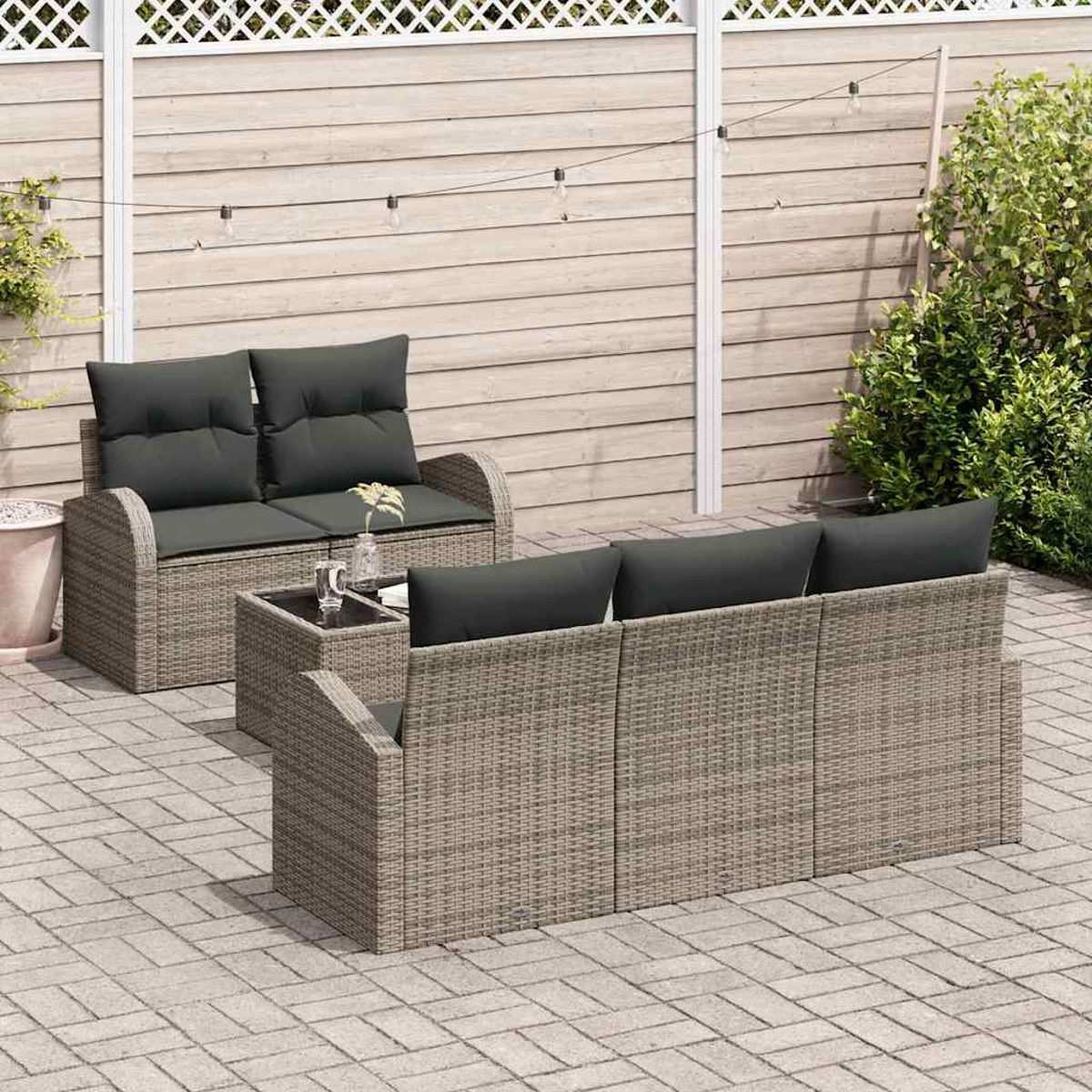 Terrassenset. Korbmöbel mit dunkelgrauen Kissen. Enthält ein Sofa, ein Sofa, einen kleinen Tisch und eine geflieste Terrasse. Hintergrund: Holzzaun.