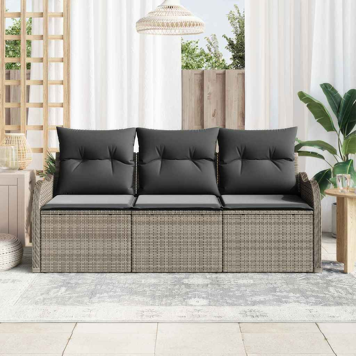 Ein Rattansofa mit grauen Kissen steht auf einem Teppich. Dahinter sind Vorhänge, ein Fenster und Pflanzen. Eine Korblampe hängt darüber.