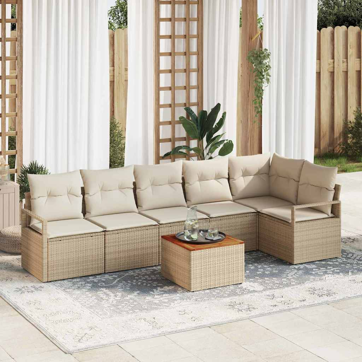 Ein Sitzbereich im Freien mit einem beigefarbenen Ecksofa, einem Holztisch und einem Teppich. Weiße Vorhänge und Pflanzen vervollständigen die Szene.