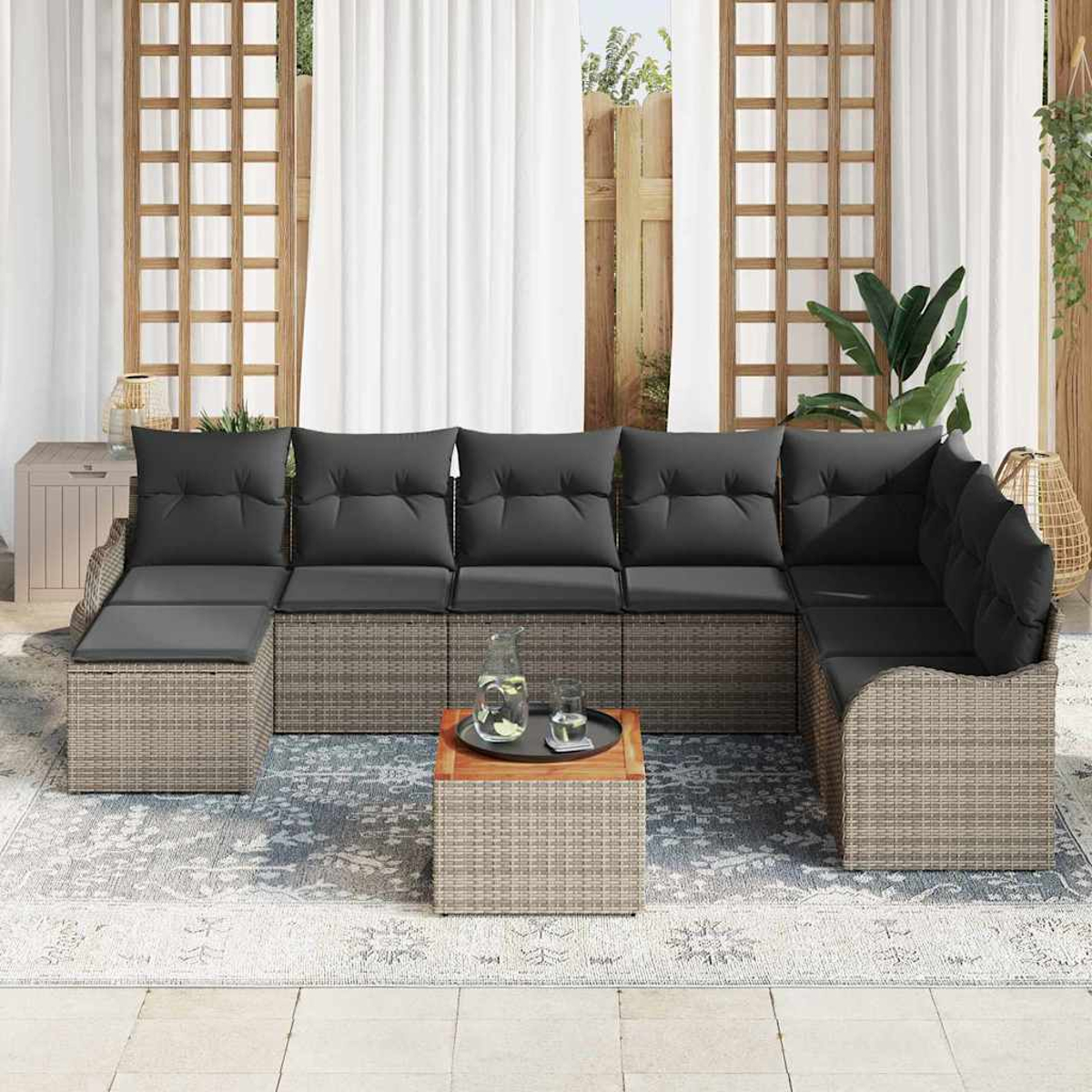 Ein Ecksofa im Freien mit grauen Kissen und einem kleinen Tisch mit Tablett auf einem gemusterten Teppich, in der Nähe eines Fensters.