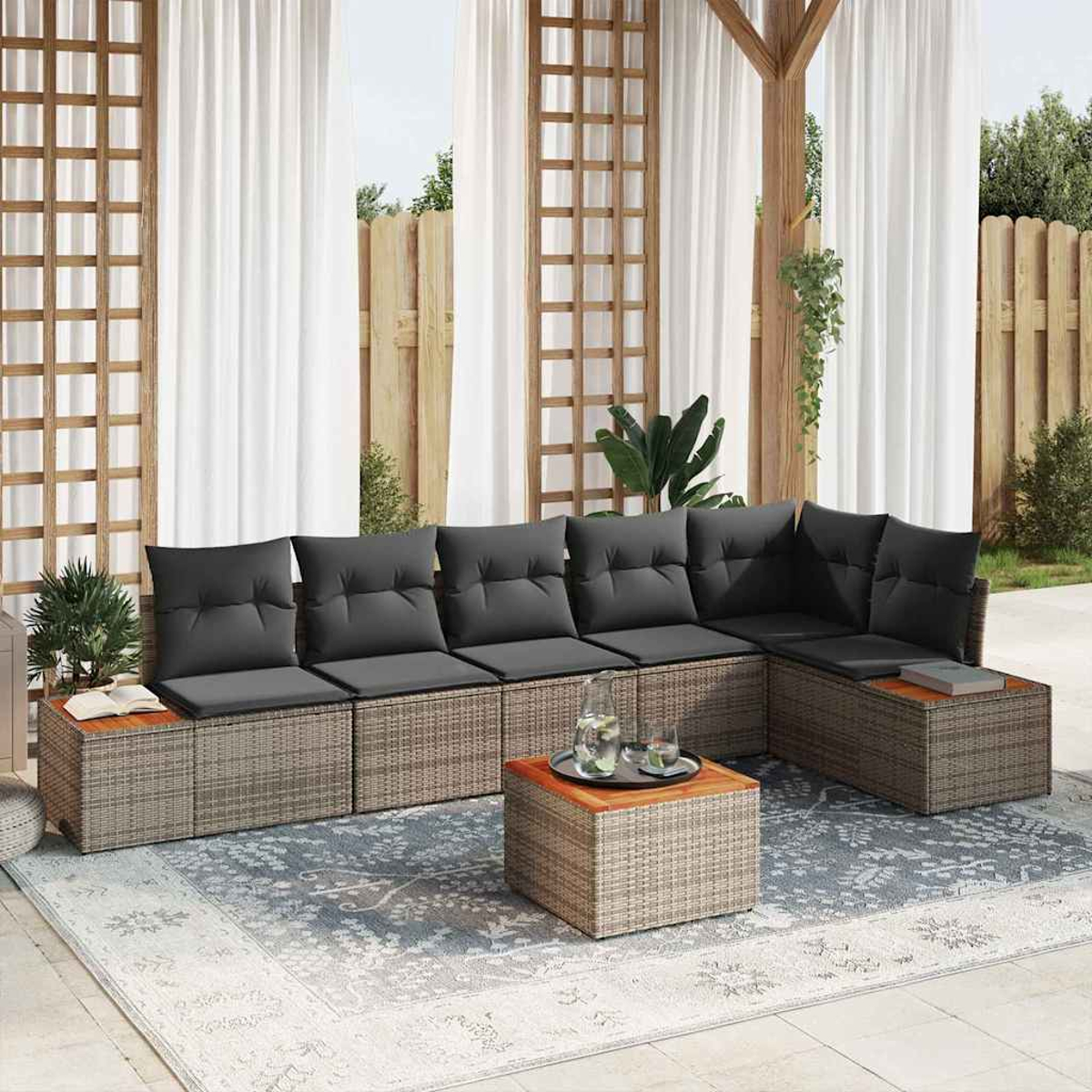 Gartenmöbelset mit grauen Kissen, einem Couchtisch und einem Teppich. Im Hintergrund Vorhänge, Holzkonstruktionen und Grün.