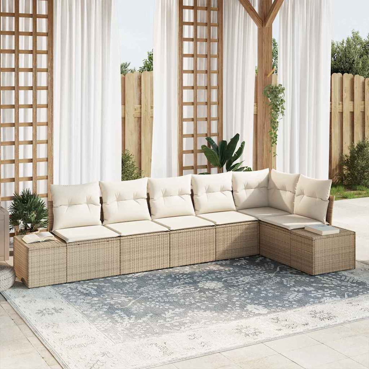 Ein Sitzbereich im Freien mit einem beigefarbenen Ecksofa, elfenbeinfarbenen Kissen und einem blau gemusterten Teppich. Weiße Vorhänge und ein Holzzaun sind im Hintergrund.