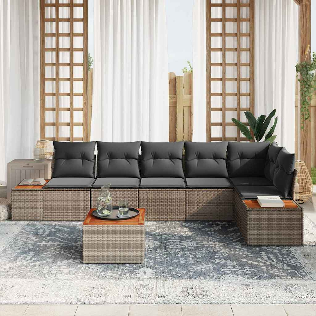 Ein Ecksofa im Freien mit grauen Kissen, zwei Holztischen und einem gemusterten Teppich. Im Hintergrund sind Vorhänge und ein Garten zu sehen.