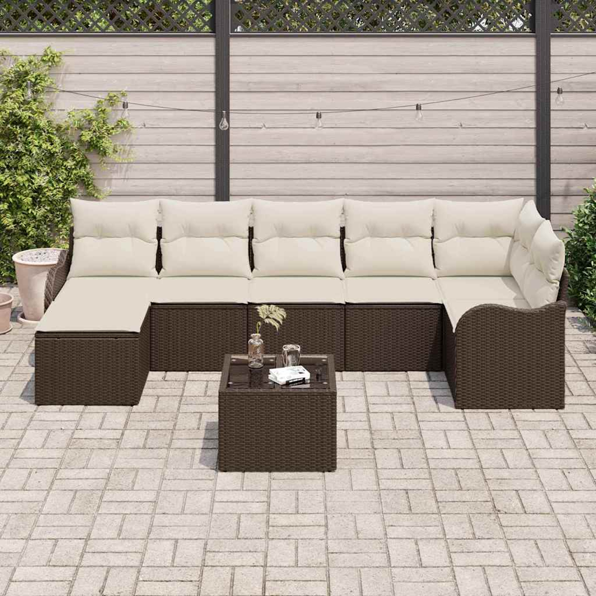 Sofá seccional exterior con cojines beige y marco de mimbre marrón, y una mesa pequeña, sobre un patio de piedra.