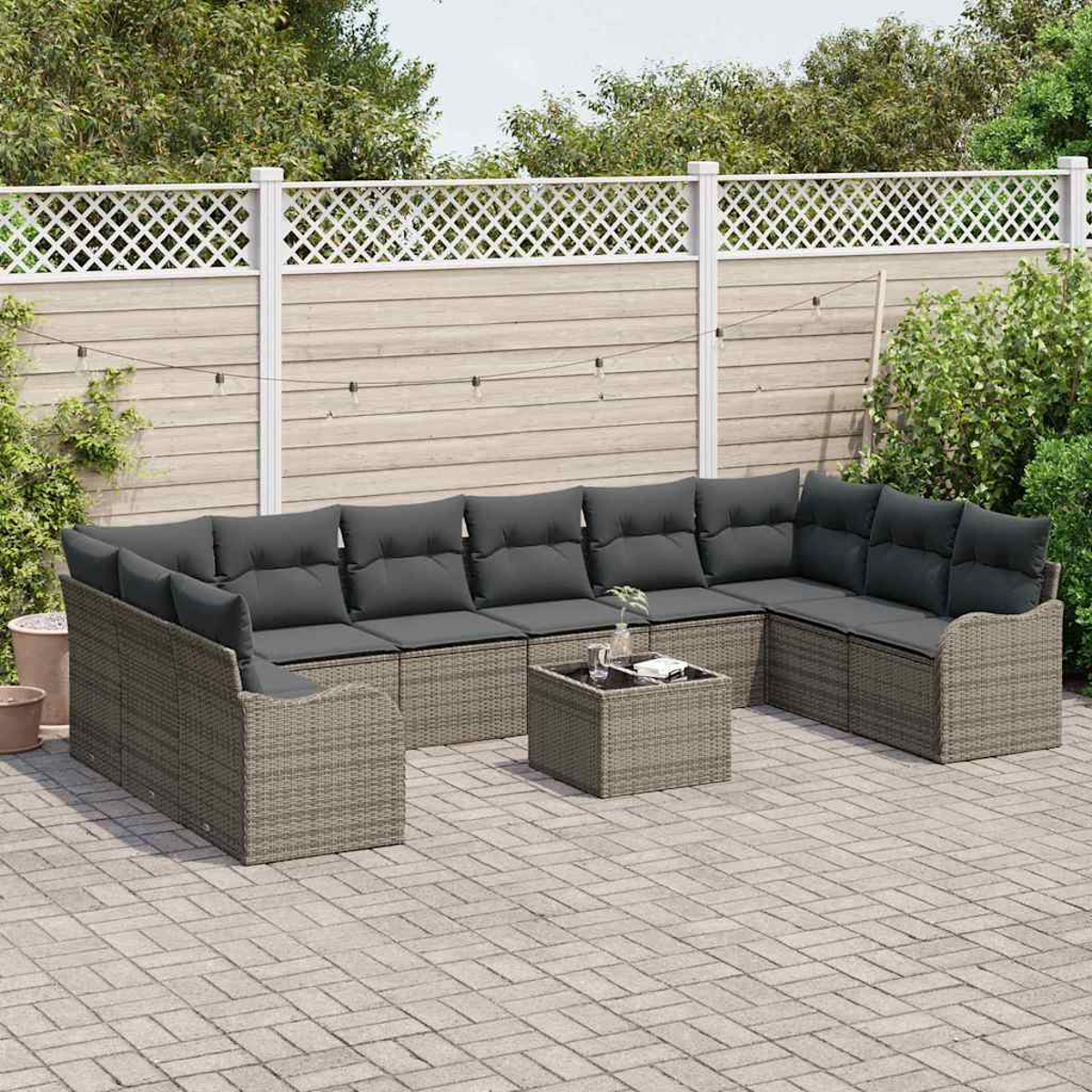 Ein graues Rattan-Ecksofa im Freien mit dunkelgrauen Kissen und einem passenden quadratischen Tisch, auf einer Backstein-Terrasse.