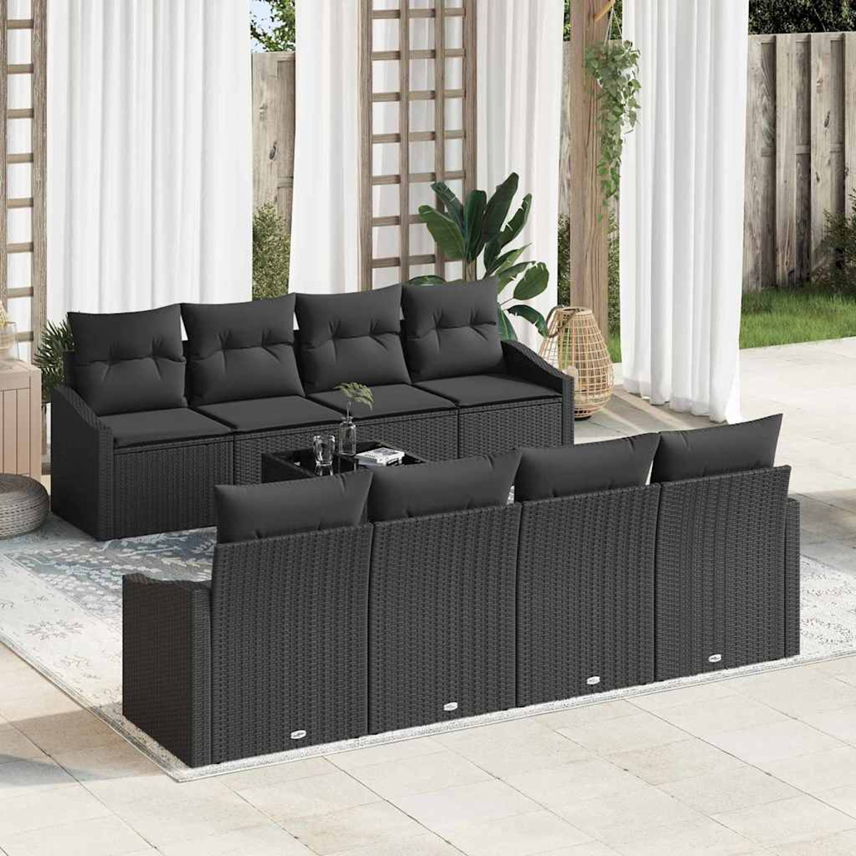 Ein schwarzes Rattan-Outdoor-Sofaset. Enthält ein großes Sofa, eine Couch und einen Couchtisch, vor weißen Vorhängen und Laub.