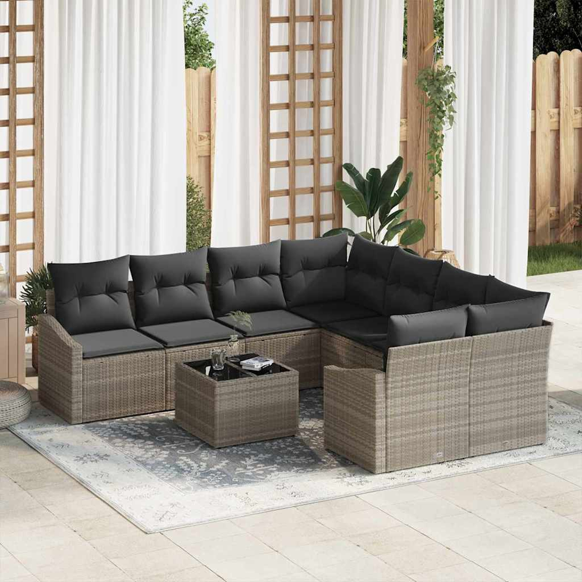 Outdoor-Ecksofa mit schwarzen Kissen und einem kleinen Tisch auf einem gemusterten Teppich auf einer Terrasse. Weiße Vorhänge im Hintergrund.