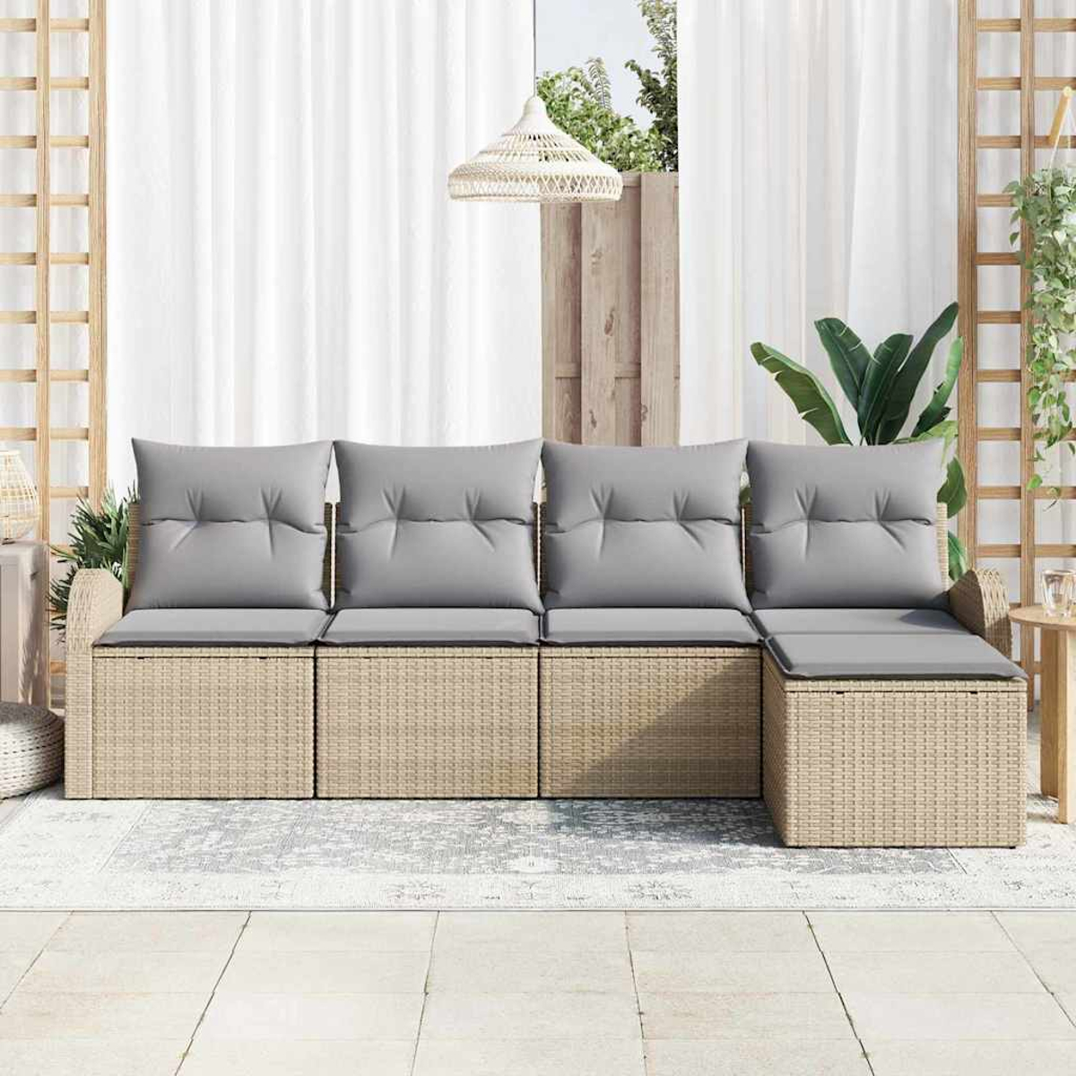 Ein Rattansofa mit grauen Kissen steht auf einer Terrasse. Weiße Vorhänge und eine Hängelampe sind im Hintergrund. Pflanzen und ein Tisch sind ebenfalls vorhanden.