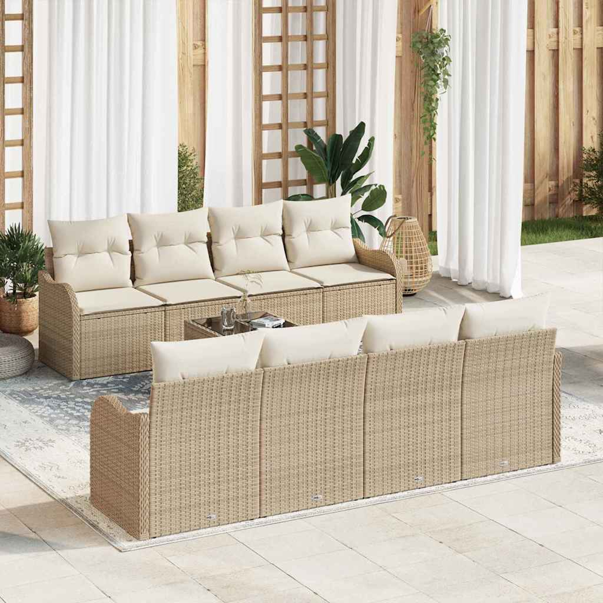 Gartenmöbel-Set aus Korbgeflecht. Beige Sofas mit cremefarbenen Kissen, Glastisch und weißen Vorhängen im Hintergrund. Pflanzen.