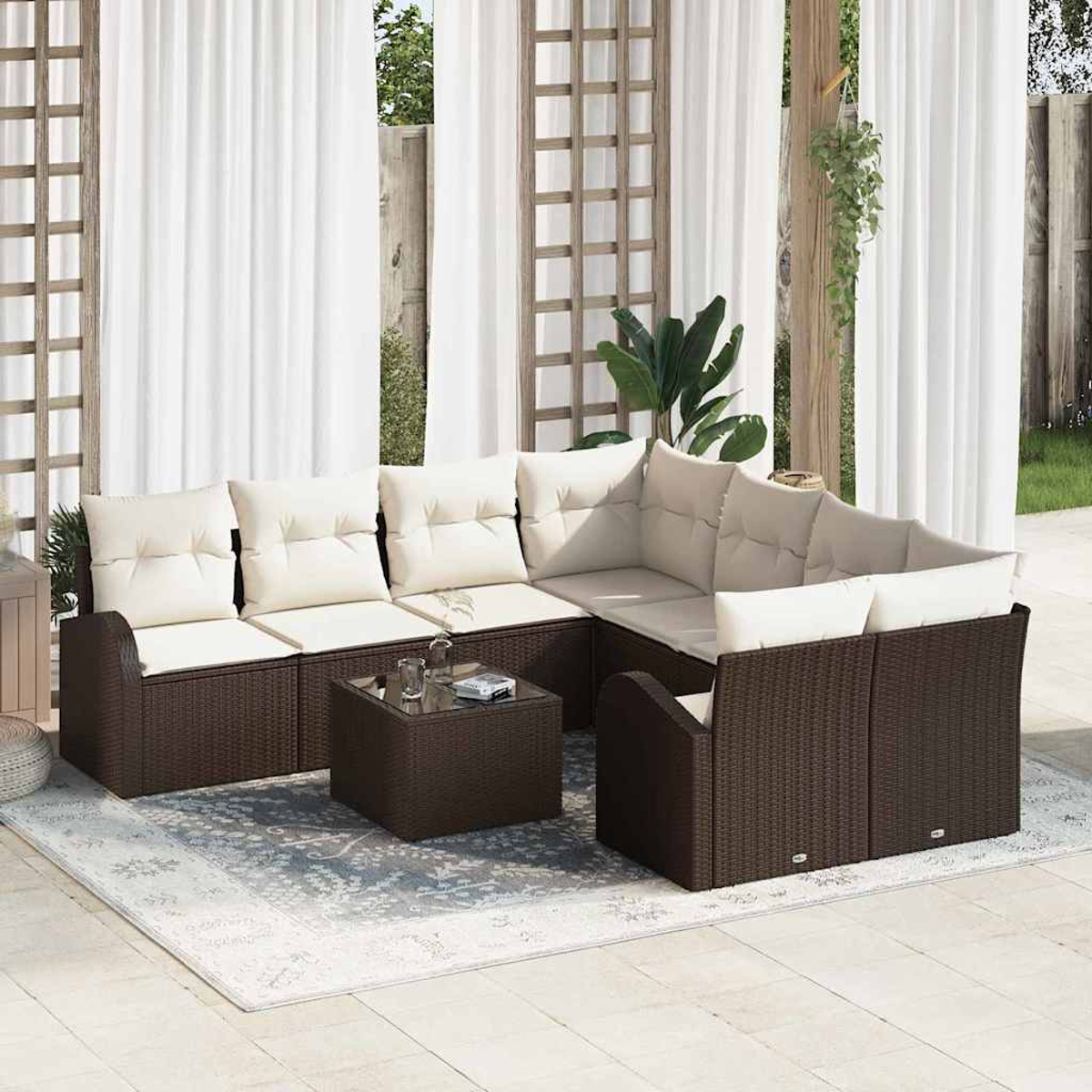 Terrassengarnitur mit braunen Korbmöbeln, cremefarbenen Kissen und einem Couchtisch mit Glasplatte. Weiße Vorhänge und ein Teppich.
