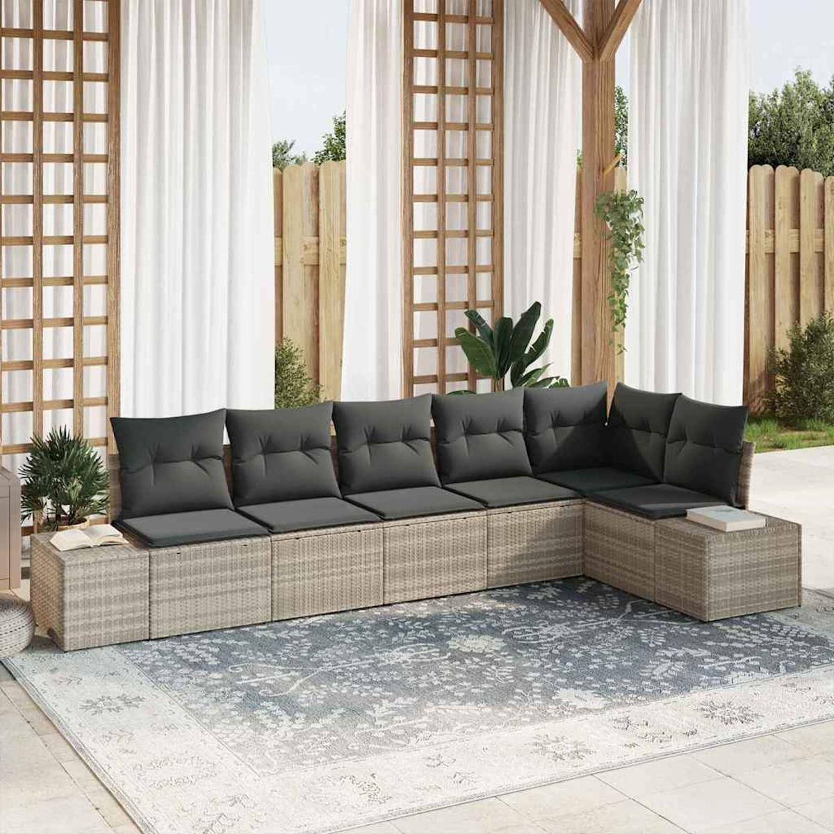 Outdoor-Ecksofa mit grauen Kissen auf einem gemusterten Teppich. Weiße Vorhänge, Holzgitter und Pflanzen im Hintergrund.