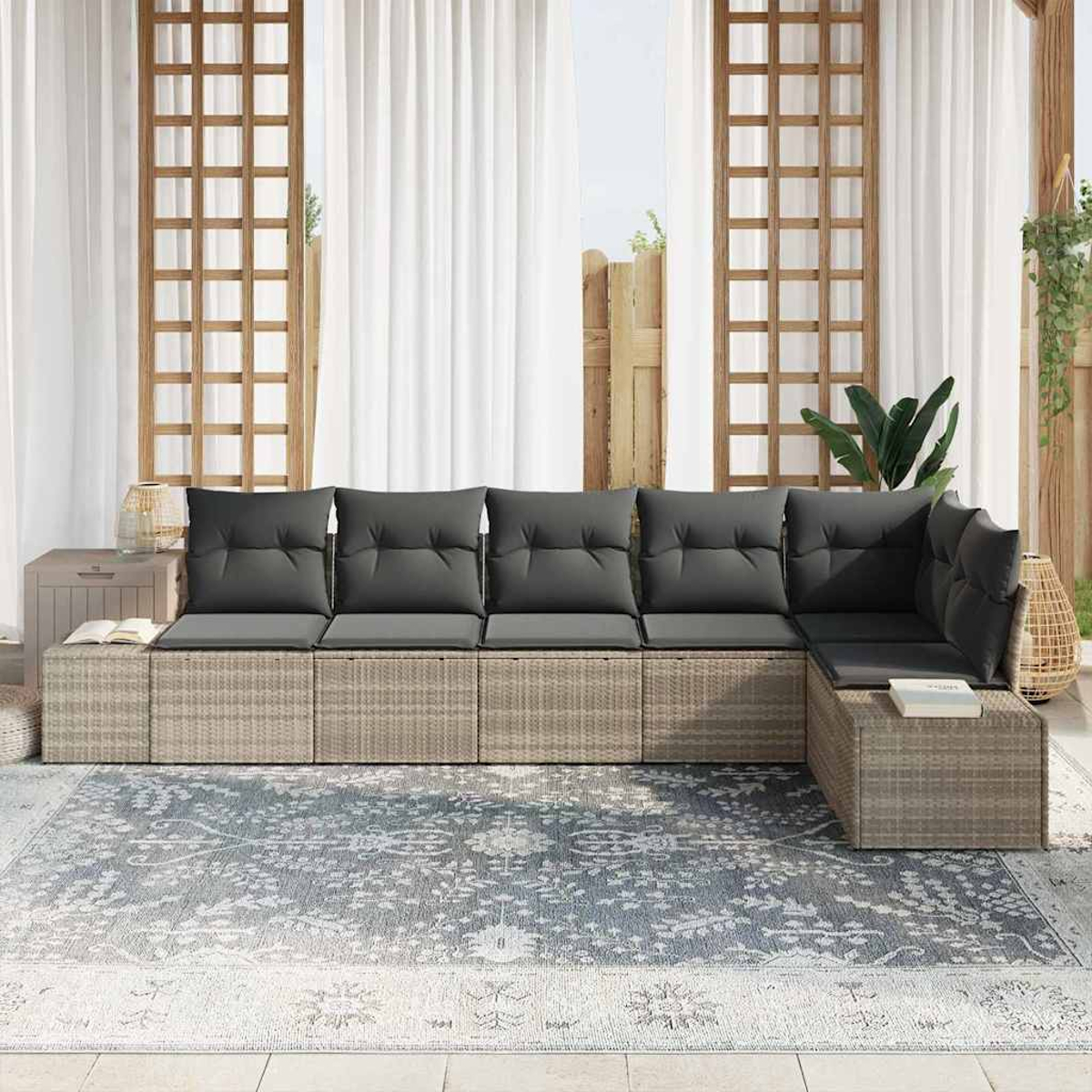 Ein Ecksofa im Freien mit grauen Kissen auf einem gemusterten Teppich, mit weißen Vorhängen und Holzgitter im Hintergrund.