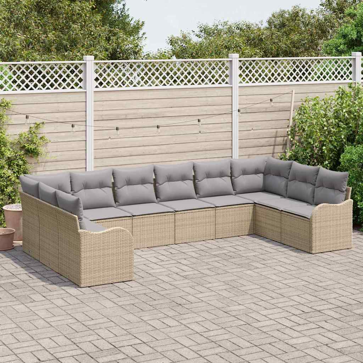 Ein beiges Korbsessel-Sofa mit grauen Kissen steht auf einer Backstein-Terrasse. Im Hintergrund ein weißer Zaun mit Grün.