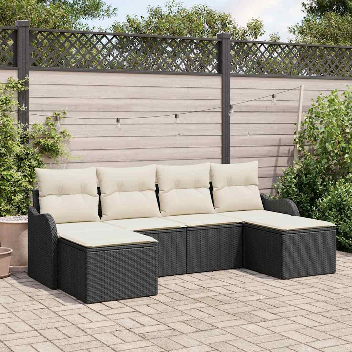 Ein schwarzes Ecksofa mit cremefarbenen Kissen steht auf einer Backsteinterrasse. Dahinter befindet sich ein Holzzaun mit dekorativem Gitter.