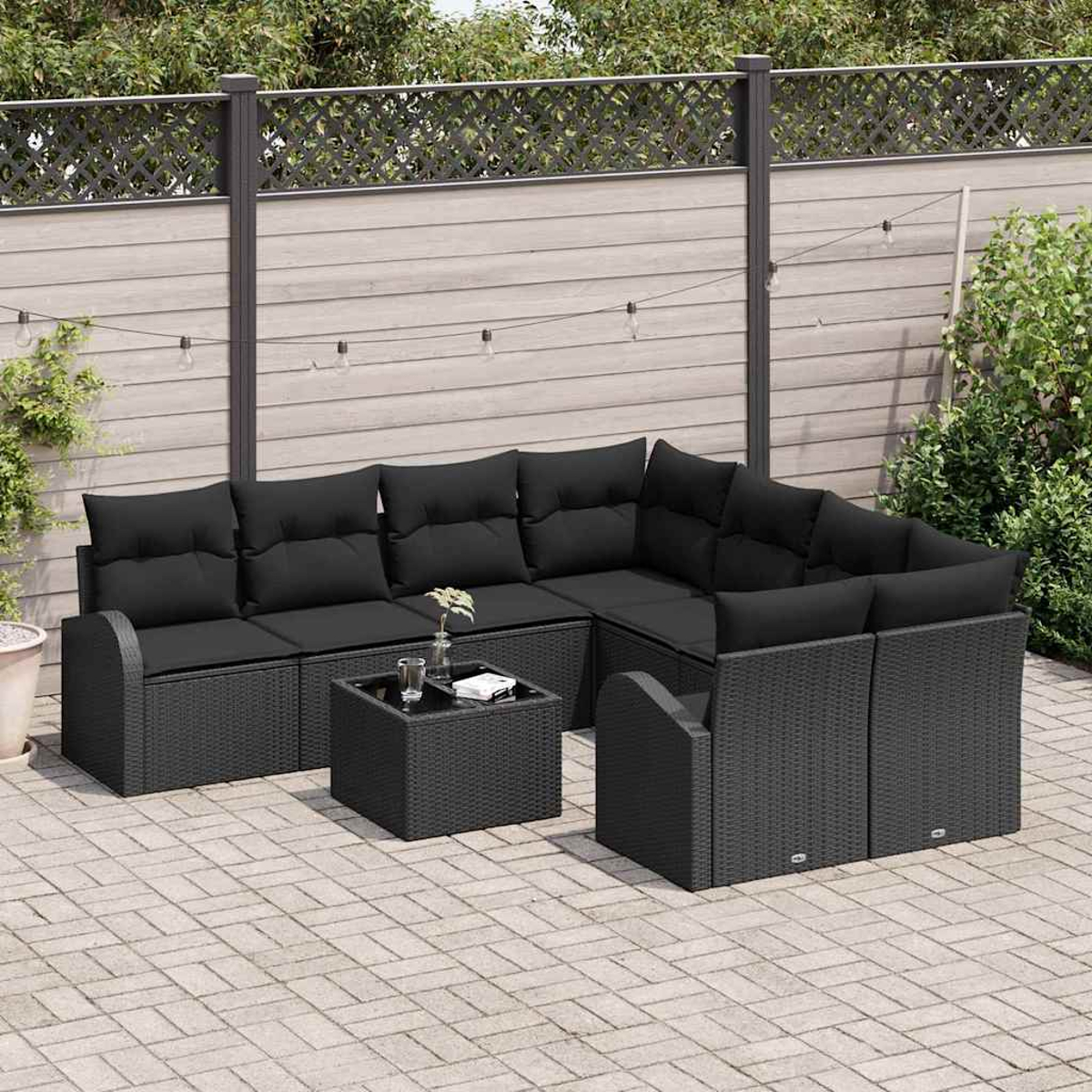 Garten-Set mit schwarzen Kissen und einem kleinen Tisch. Es ist ein Ecksofa und ein Stuhl auf einer gepflasterten Terrasse.