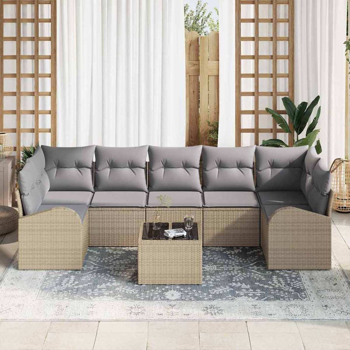 Outdoor-Ecksofa mit grauen Kissen und einem kleinen Tisch steht auf einem Teppich. Weiße Vorhänge und Holzgitter im Hintergrund.